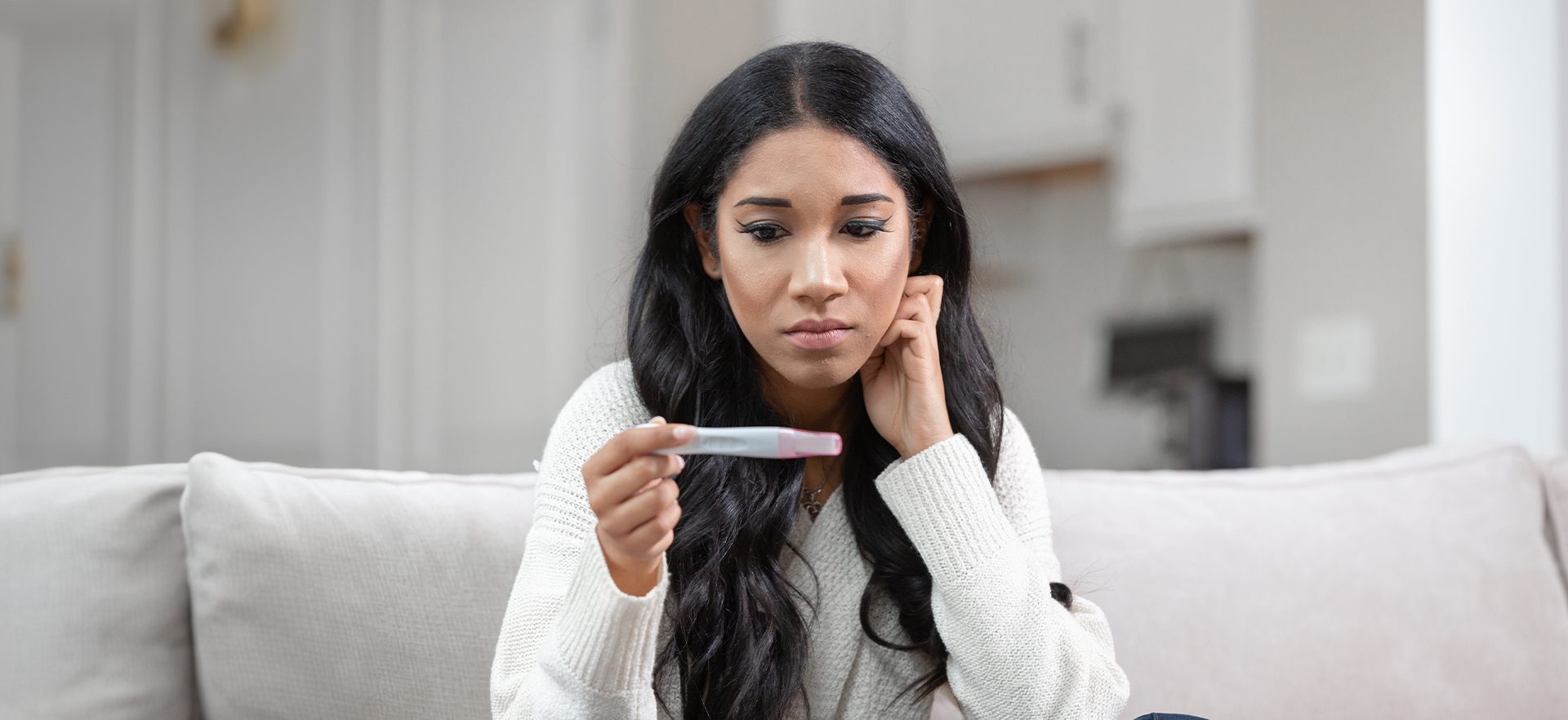 young racially ambiguous woman looking at a positive pregnancy test