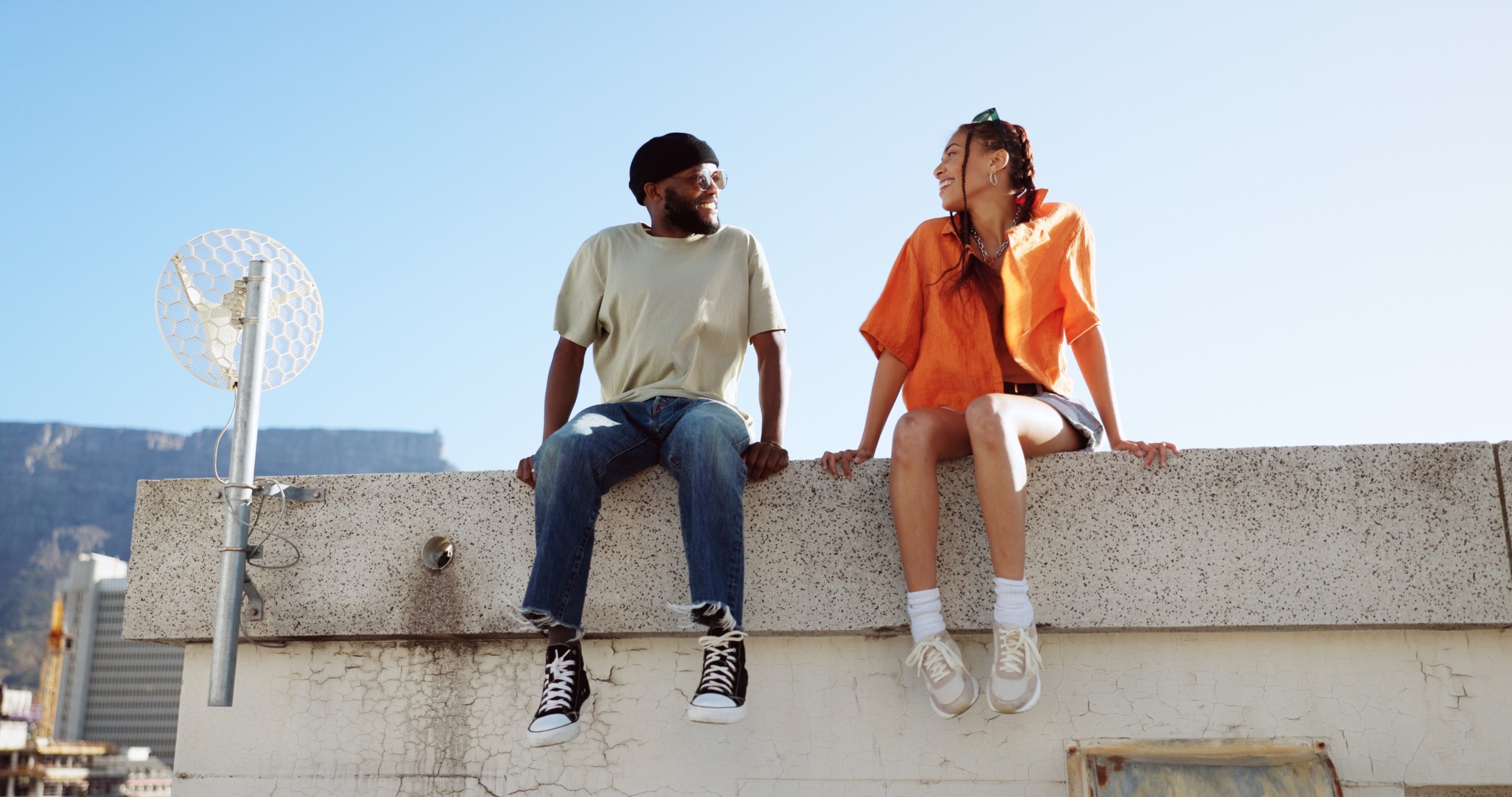 young african american couple sitting on a edge of a cement wall looking at each other